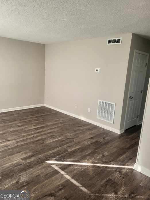 unfurnished room featuring dark wood-type flooring and a textured ceiling