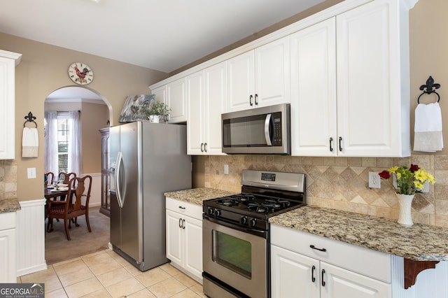 kitchen featuring light tile patterned floors, stainless steel appliances, light stone countertops, decorative backsplash, and white cabinets