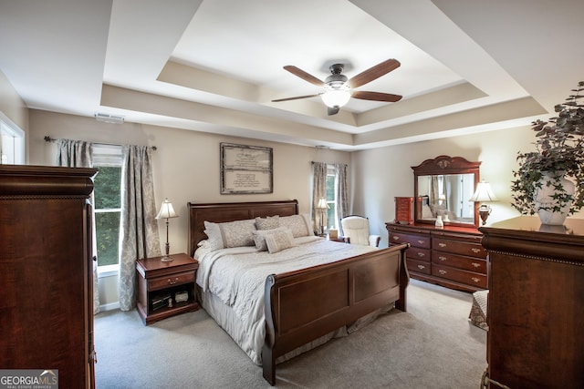 bedroom featuring a raised ceiling, light carpet, ceiling fan, and multiple windows