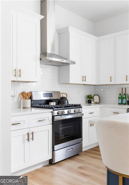 kitchen featuring stainless steel range with gas stovetop, white cabinetry, wall chimney range hood, and light hardwood / wood-style flooring