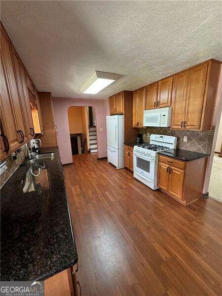 kitchen featuring dark wood-type flooring, decorative backsplash, sink, and white appliances