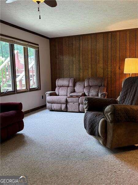 living room featuring ceiling fan, a textured ceiling, wooden walls, and carpet flooring