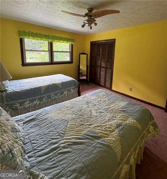 carpeted bedroom with a textured ceiling, ceiling fan, and a closet