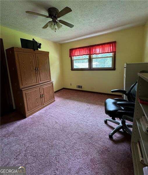 carpeted office with a textured ceiling and ceiling fan