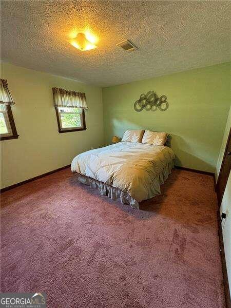 bedroom featuring a textured ceiling, multiple windows, and carpet flooring