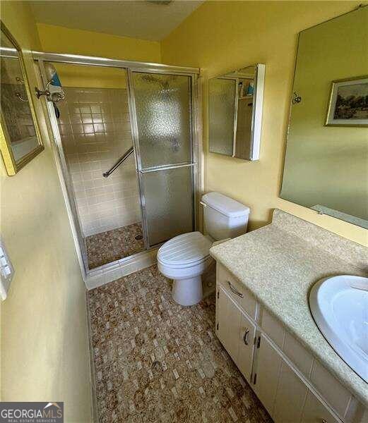 bathroom with tile patterned floors, a shower with shower door, toilet, and vanity