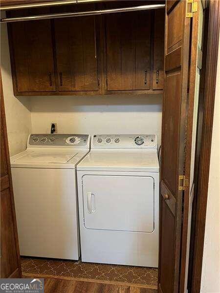 clothes washing area with washer and dryer, dark hardwood / wood-style flooring, and cabinets