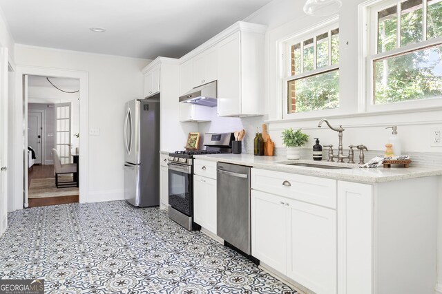 kitchen with appliances with stainless steel finishes, white cabinets, sink, and light stone counters