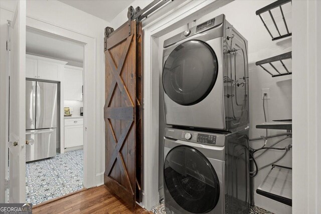 laundry room with stacked washer / drying machine, a barn door, and wood-type flooring