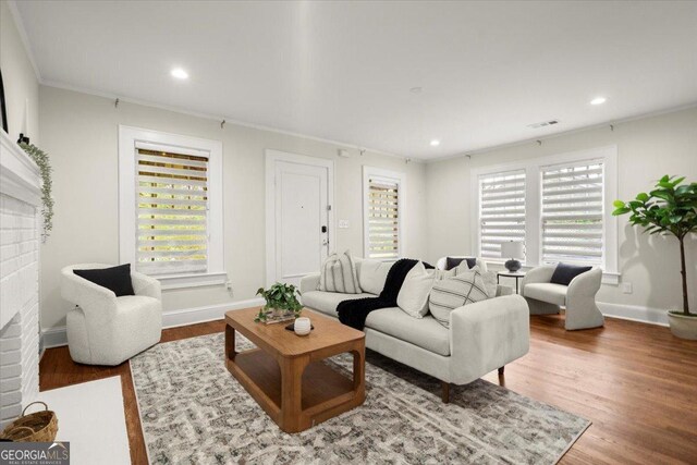 living room with wood-type flooring, ornamental molding, and a brick fireplace