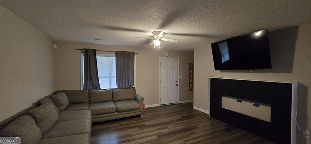 living room featuring ceiling fan, a fireplace, dark hardwood / wood-style floors, and a textured ceiling