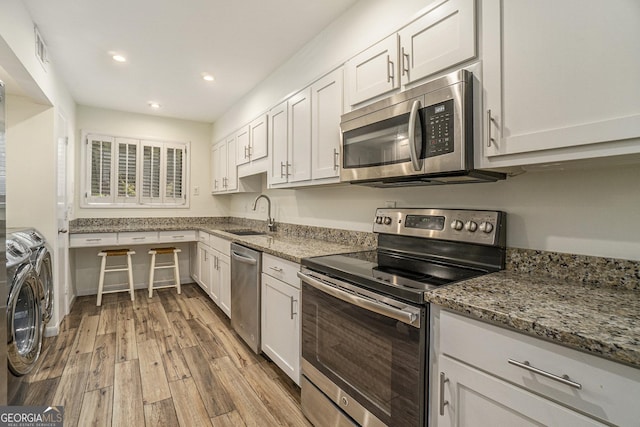 kitchen with appliances with stainless steel finishes, sink, washer and dryer, and white cabinets