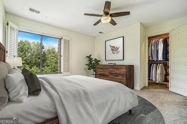 bedroom featuring a spacious closet, light carpet, ceiling fan, and a closet