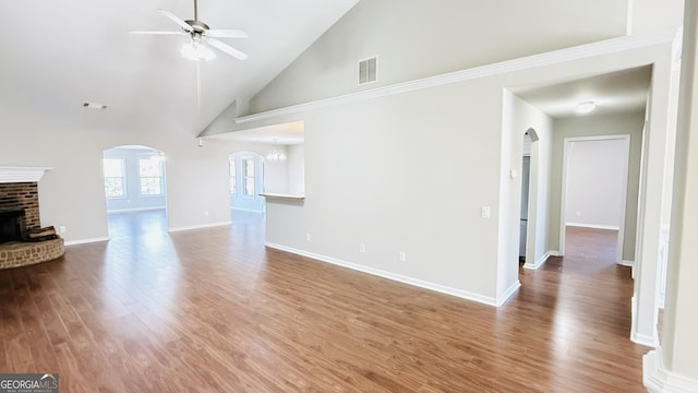 unfurnished living room featuring arched walkways, a ceiling fan, a brick fireplace, wood finished floors, and baseboards