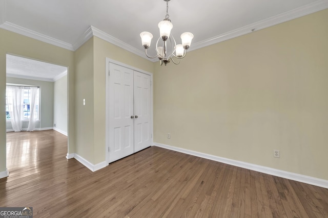 unfurnished dining area with baseboards, a chandelier, wood finished floors, and crown molding