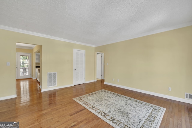 interior space with a textured ceiling, wood finished floors, visible vents, and crown molding