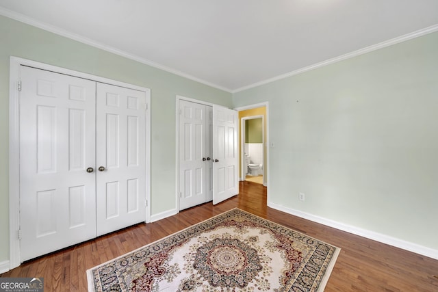 bedroom featuring multiple closets, crown molding, baseboards, and wood finished floors