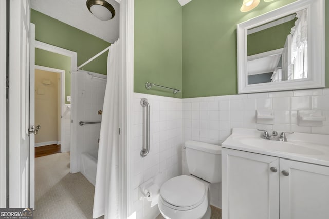 bathroom with toilet, a wainscoted wall, shower / bath combination with curtain, vanity, and tile walls