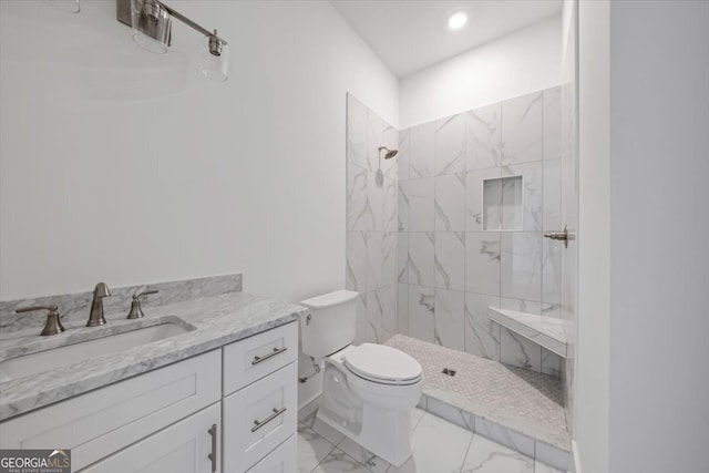 bathroom with a tile shower, vanity, and toilet