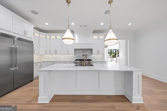 kitchen with white cabinets, a center island with sink, and built in fridge