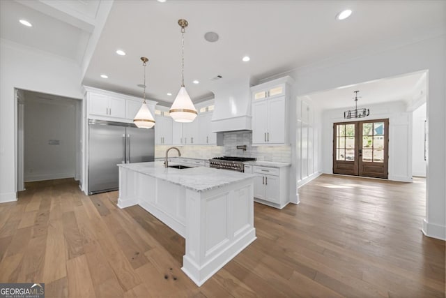 kitchen with white cabinets, an island with sink, stainless steel appliances, and light hardwood / wood-style floors