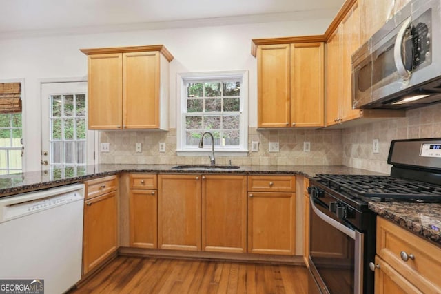 kitchen featuring sink, crown molding, stainless steel appliances, dark stone counters, and light wood-type flooring