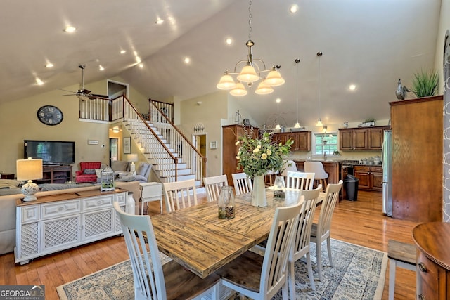 dining room with high vaulted ceiling, sink, ceiling fan with notable chandelier, and light wood-type flooring