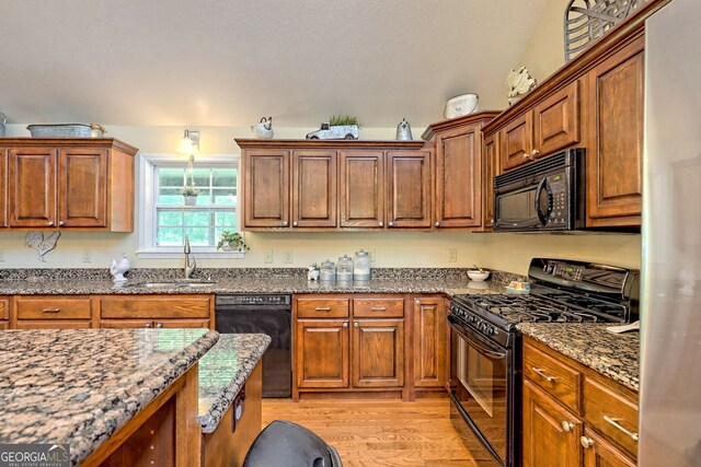 kitchen featuring sink, black appliances, light wood-type flooring, and dark stone counters