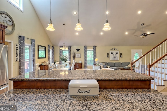 kitchen featuring dark stone countertops, stainless steel refrigerator, ceiling fan, decorative light fixtures, and high vaulted ceiling