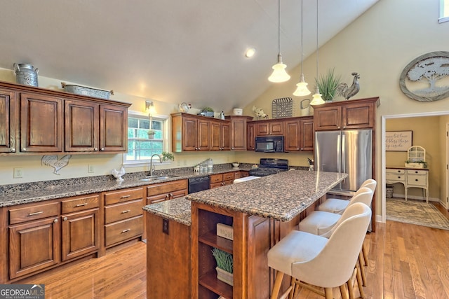 kitchen with sink, dark stone countertops, a center island, black appliances, and decorative light fixtures