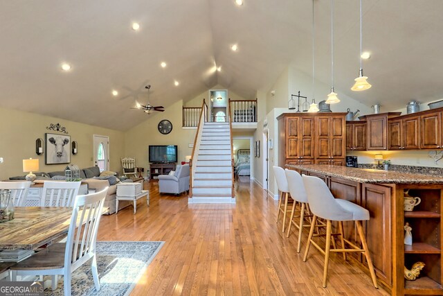 kitchen featuring ceiling fan, light hardwood / wood-style floors, stone countertops, a kitchen breakfast bar, and high vaulted ceiling