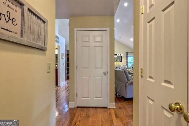 hallway featuring an inviting chandelier, lofted ceiling, and hardwood / wood-style floors