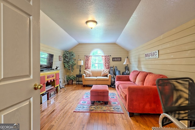 living room featuring lofted ceiling, wooden walls, hardwood / wood-style floors, and a textured ceiling