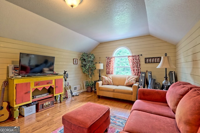 living room featuring lofted ceiling, a textured ceiling, light wood-type flooring, and wood walls