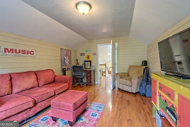 living room featuring vaulted ceiling, wooden walls, light wood-type flooring, and a textured ceiling