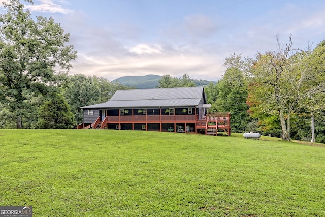 back house at dusk featuring a wooden deck and a lawn