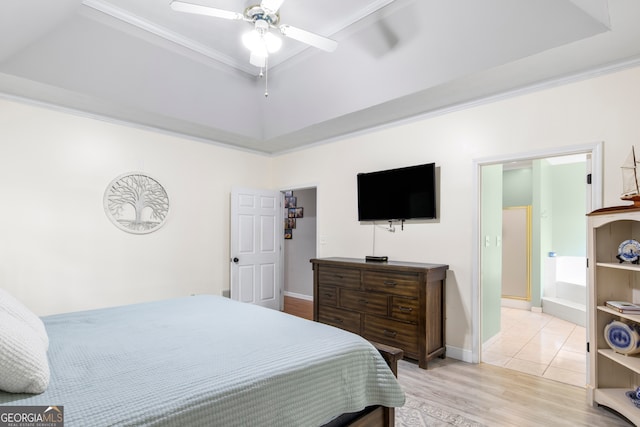 bedroom featuring ceiling fan, ensuite bath, ornamental molding, a raised ceiling, and light hardwood / wood-style floors