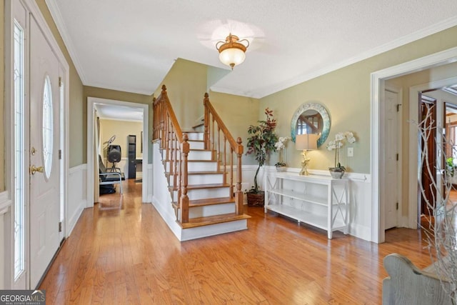 foyer entrance with a wealth of natural light, crown molding, and light hardwood / wood-style flooring