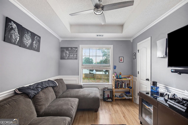 living room with light hardwood / wood-style flooring, a textured ceiling, ceiling fan, a raised ceiling, and ornamental molding