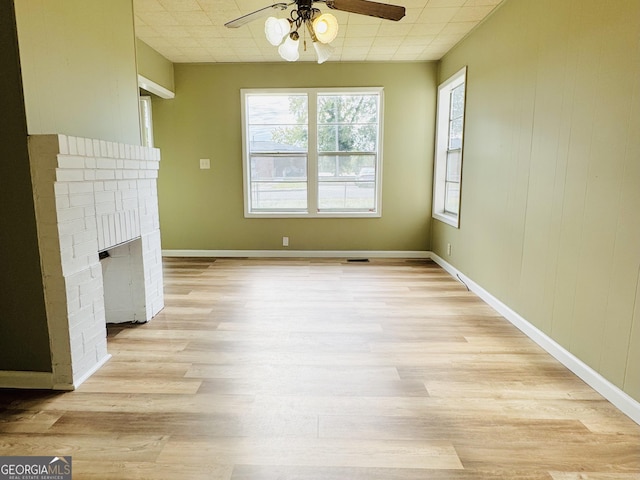 unfurnished dining area featuring a brick fireplace, ceiling fan, and light hardwood / wood-style floors