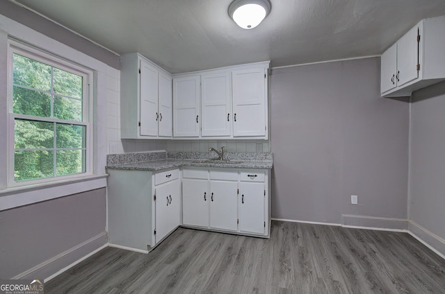 kitchen featuring white cabinets, wood-type flooring, light stone counters, and sink