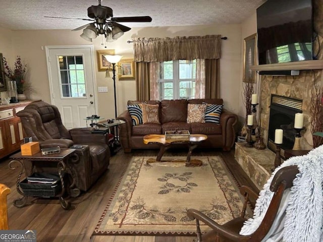 living area featuring ceiling fan, a fireplace, a textured ceiling, and wood finished floors