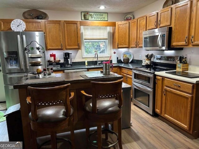 kitchen with a textured ceiling, stainless steel appliances, a breakfast bar, brown cabinets, and light wood finished floors