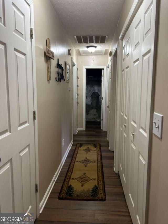 hall featuring a textured ceiling, wood finished floors, visible vents, and baseboards