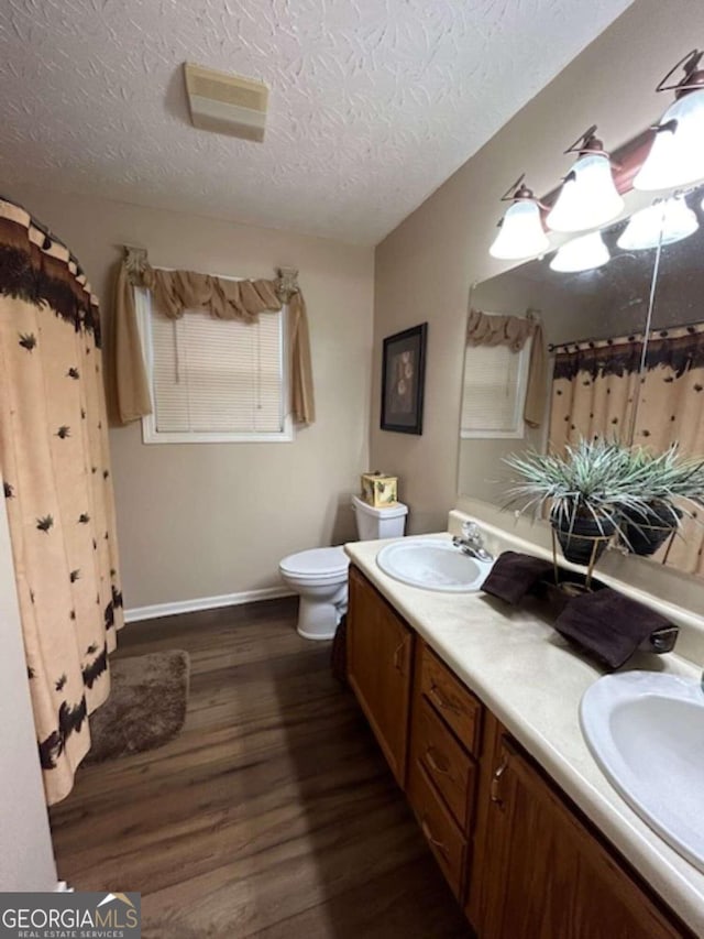 full bathroom featuring toilet, double vanity, a sink, and wood finished floors