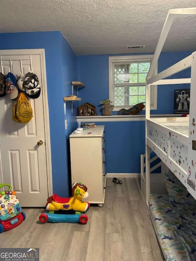 bedroom with a textured ceiling, wood finished floors, and visible vents