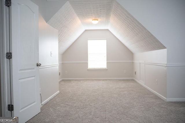 additional living space with vaulted ceiling, light colored carpet, and a textured ceiling