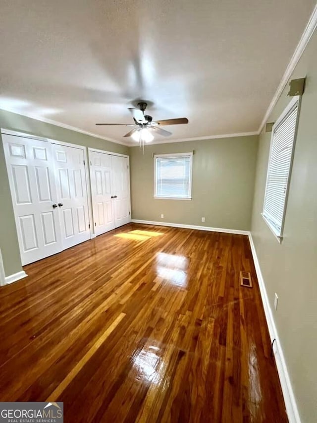 unfurnished bedroom featuring multiple closets, ceiling fan, wood-type flooring, and crown molding