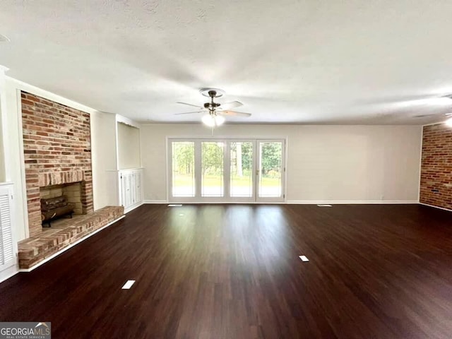 unfurnished living room featuring a fireplace, dark hardwood / wood-style floors, ceiling fan, and brick wall