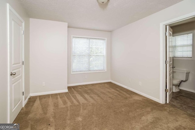 unfurnished bedroom with carpet, ensuite bath, and a textured ceiling